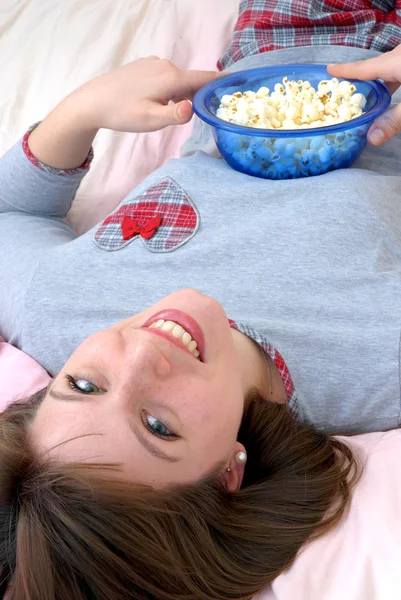 Hermosa joven caucásica mujer disfrutando de comer palomitas de maíz en su cama . — Foto de Stock