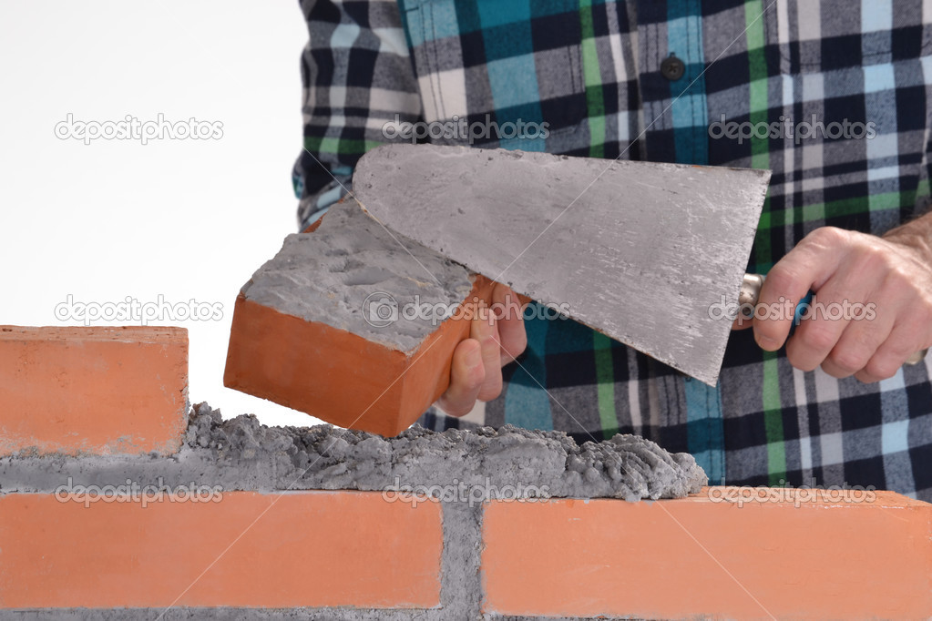 Constructor hand holding a brick and building a wall.