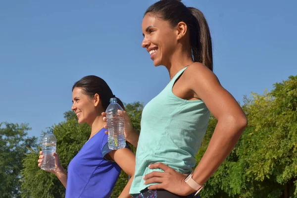 Две Молодые Латинские Женщины Пьют Бутылку Воды После Тренировки Голубом — стоковое фото