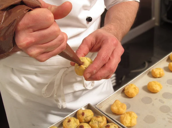 Pastry chef preparing and making chocolate sweets using cream pastry bag