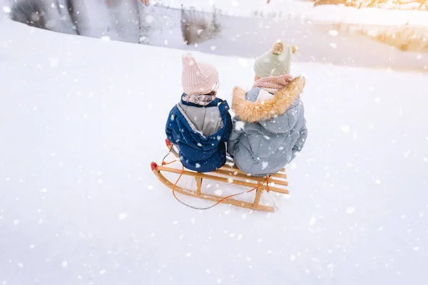 Deux enfants montent sur luge rétro en bois le jour ensoleillé de l'hiver. Jeux actifs d'hiver en plein air. Activités hivernales pour les enfants. Enfants jouant avec la neige dans le parc. — Photo