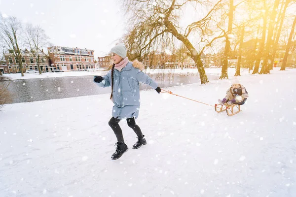 Deux enfants montent sur luge rétro en bois le jour ensoleillé de l'hiver. Jeux actifs d'hiver en plein air. Activités hivernales pour les enfants. Enfants jouant avec la neige dans le parc. — Photo