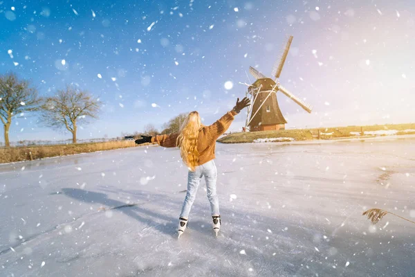 Fille s'amuser sur la glace dans un paysage typique hollandais avec moulin à vent. Femme patiner sur la patinoire à l'extérieur par une journée ensoleillée et enneigée. Activité de plein air sur canal gelé en hiver Réveillon de Noël — Photo