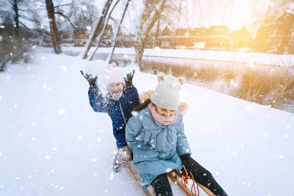 Deux enfants montent sur luge rétro en bois le jour ensoleillé de l'hiver. Jeux actifs d'hiver en plein air. Activités hivernales pour les enfants. Enfants jouant avec la neige dans le parc. — Photo