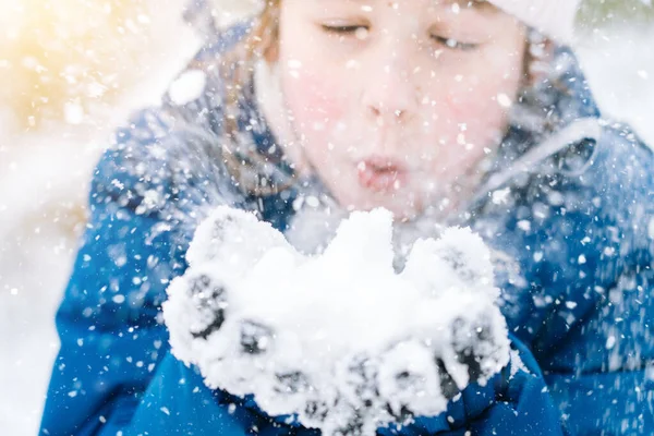 Girl playing on snow in winter time. Happy children in beautiful snowy winter forest on Christmas day. girl blows snow on snowflakes bokeh background. Royalty Free Stock Photos