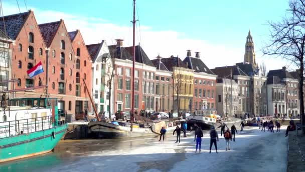 人々はオランダの都市中心部の冷凍運河でアイススケートをします。冬には氷結した運河で写真を撮り、歩き、スケートをする人々。市内の冬の楽しみGroningen 。オランダだ。14.02.2021. — ストック動画