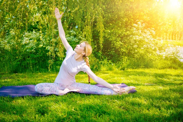 Parkta yoga yapan genç bir kadın. Kız yoga pozisyonunda egzersiz yapıyor. Nilüfer pozisyonunda oturup yoga yapan mutlu ve sağlıklı bir kadın. Gün batımında meditasyon ve spor.