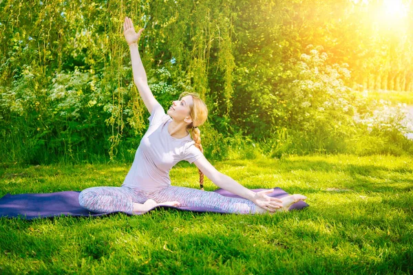 Mujer joven haciendo yoga asana en parque. chica estirando ejercicio en posición de yoga. mujer feliz y saludable sentada en posición de loto y practicando yoga. meditación y deporte al atardecer al aire libre. Imágenes De Stock Sin Royalties Gratis