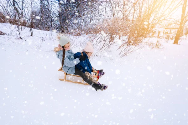 Deux enfants montent sur luge rétro en bois le jour ensoleillé de l'hiver. Jeux actifs d'hiver en plein air. Activités hivernales pour les enfants. Enfants jouant avec la neige dans le parc. — Photo