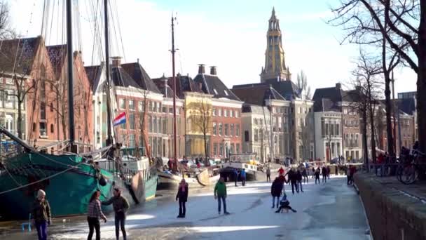 İnsanlar Hollanda 'nın merkezindeki donmuş kanalda buz pateni yapıyorlar. İnsanlar kışın donmuş kanalda resim yapıyor, yürüyor ve paten kayıyor. Groningen şehrinde kış eğlencesi. Hollanda 'da. 14.02.2021. — Stok video