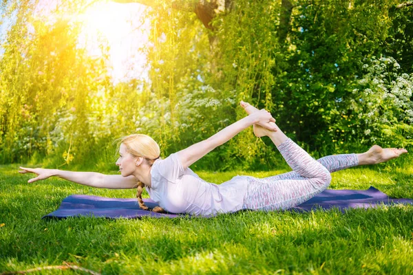 Jovem mulher fazendo ioga asana no parque. exercício de alongamento menina na posição de ioga. mulher feliz e saudável sentada em posição de lótus e praticando ioga. meditação e esporte ao pôr do sol ao ar livre. — Fotografia de Stock