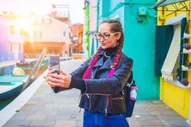 Gezgin blogcu Venedik lagünündeki Burano adasında renkli evlerin yakınında selfie çekiyor. İtalya 'da seyahat ve tatil kavramı. Güzel İtalyan şehrinde hayat tarzı seyahat anları