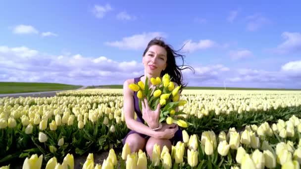 Hermosa mujer en vestido de verano de pie en coloridos campos de flores de tulipán en la región de Amsterdam, Holanda, Países Bajos. Paisaje mágico de Holanda con campo de tulipanes en Holanda Trevel y concepto de primavera — Vídeo de stock