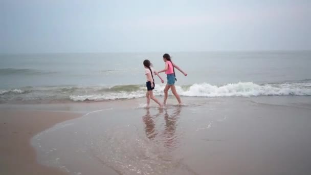 Beautiful girls playing at tropical beach. Kids enjoying warm splashing sea. Children having fun and jumping in sea water on waves on warm sunny day on seashore. Summer travel and vacation concept — Vídeo de Stock