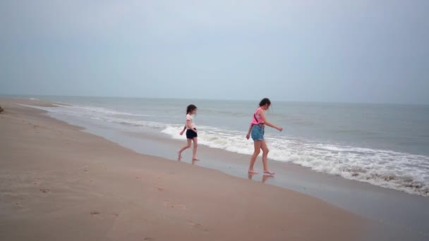 Hermosas chicas jugando en la playa tropical. A los niños les gusta el mar caliente. Los niños se divierten y saltan en el agua de mar en las olas en un día cálido y soleado en la orilla del mar. Viajes de verano y concepto de vacaciones — Vídeos de Stock