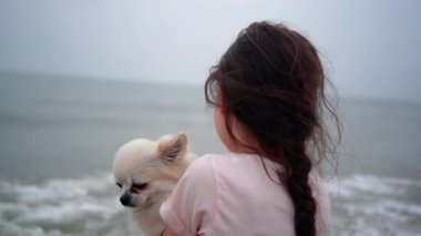 Mutlu kız deniz kıyısında mavi gökyüzüne karşı küçük köpeğine sarılıyor. En iyi arkadaşlar dinlenir ve tatilde eğlenir. Yaz konsepti