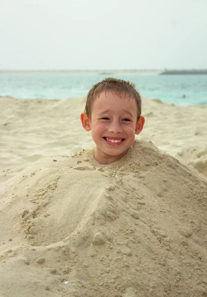 The child on a beach in a heap of sand, behind it the sea — Stock Photo, Image