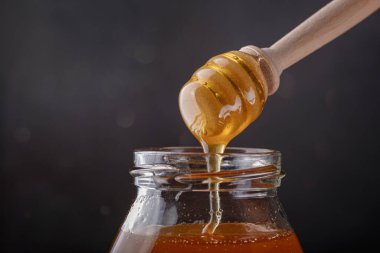 Cam kavanozdan bal damlıyor, yakın plan. Ahşap bal kaşığından daldırılan sağlıklı organik bal, yakın plan..