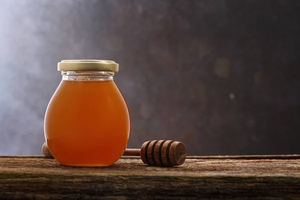 Honey background. Sweet honey in the comb, glass jar and a spoon for honey on the table. Darck background.