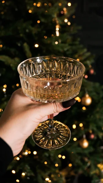 Hand holding stylish vintage wine glass on background of christmas tree lights — Stock Photo, Image