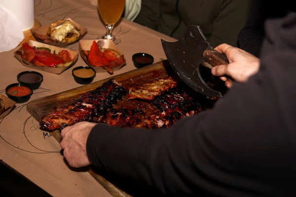 Waiter chops juicy barbecue ribs when serving to restaurant customers — Zdjęcie stockowe