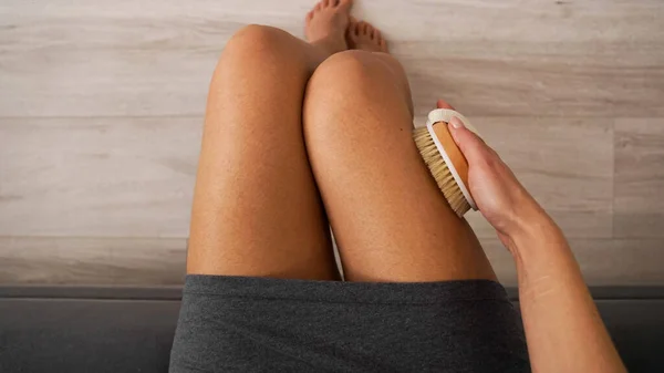 Mujer sosteniendo cepillo de madera y haciendo masaje seco en sus piernas. Concepto de autocuidado — Foto de Stock