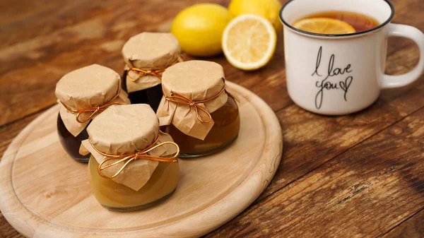 Sweet breakfast. Cup of black tea with lemon. Lemons and four jars with jam — Stock Photo, Image