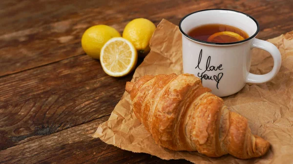 Croissants frais et une tasse de thé au citron sur une table en bois. Vue du dessus — Photo
