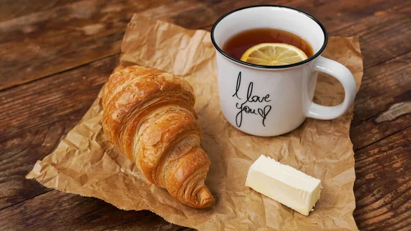 Croissants frais au beurre et une tasse de thé au citron sur une table en bois — Photo