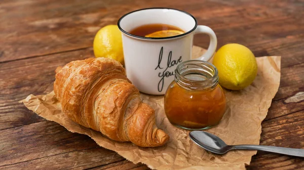 Thé au citron, confiture maison, croissant sur table en bois. Concept petit déjeuner. — Photo