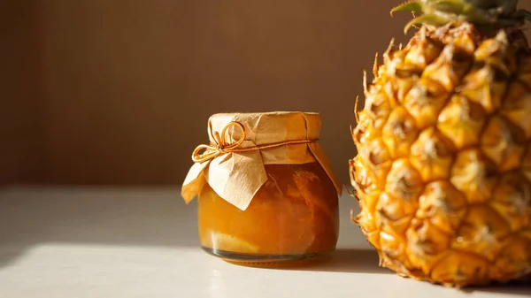 Pineapple jam in glass jar and fresh pineapple fruit with hard shadows — Stock Photo, Image