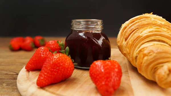 Mermelada de fresa en frasco de vidrio con bayas frescas, croissant sobre fondo de madera —  Fotos de Stock