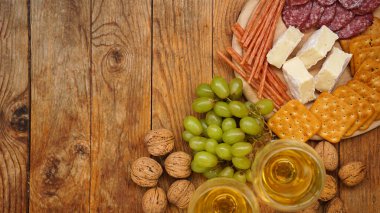 Şarap için atıştırmalıklar. Peynir ve et tabağı. Sosis, peynir, fındık, üzüm, ahşap arka planda kraker. Üst görünüm, metin için boşluk