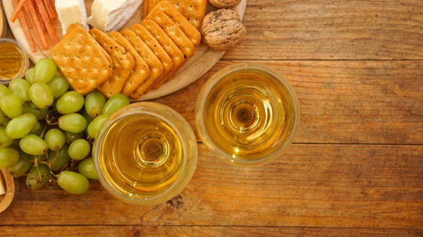 Uve verdi, cracker, noci e due bicchieri di vino bianco su fondo di legno — Foto Stock