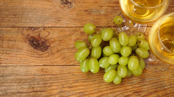 Una rama de uvas verdes y dos copas de vino blanco sobre un fondo de madera —  Fotos de Stock