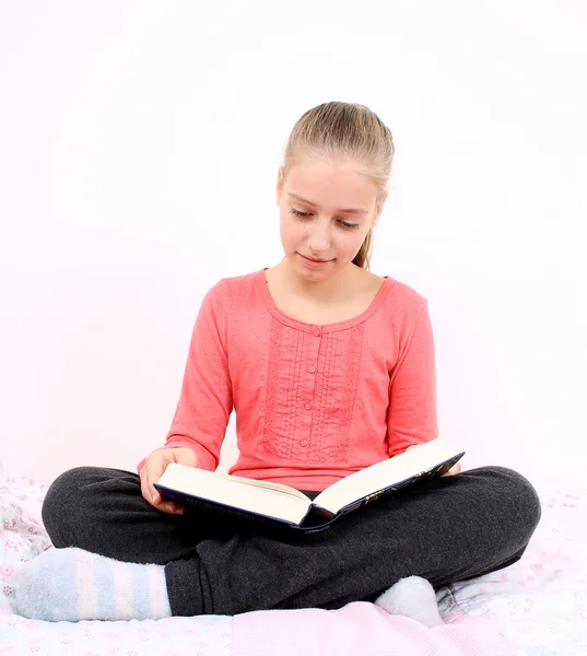 Blond girl reads interesting book sitting on bed — Stock Photo, Image