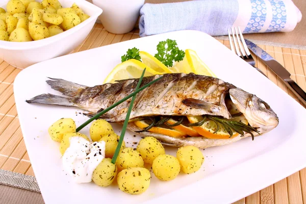 Peixe grelhado inteiro servido com batatas, limão e molho — Fotografia de Stock