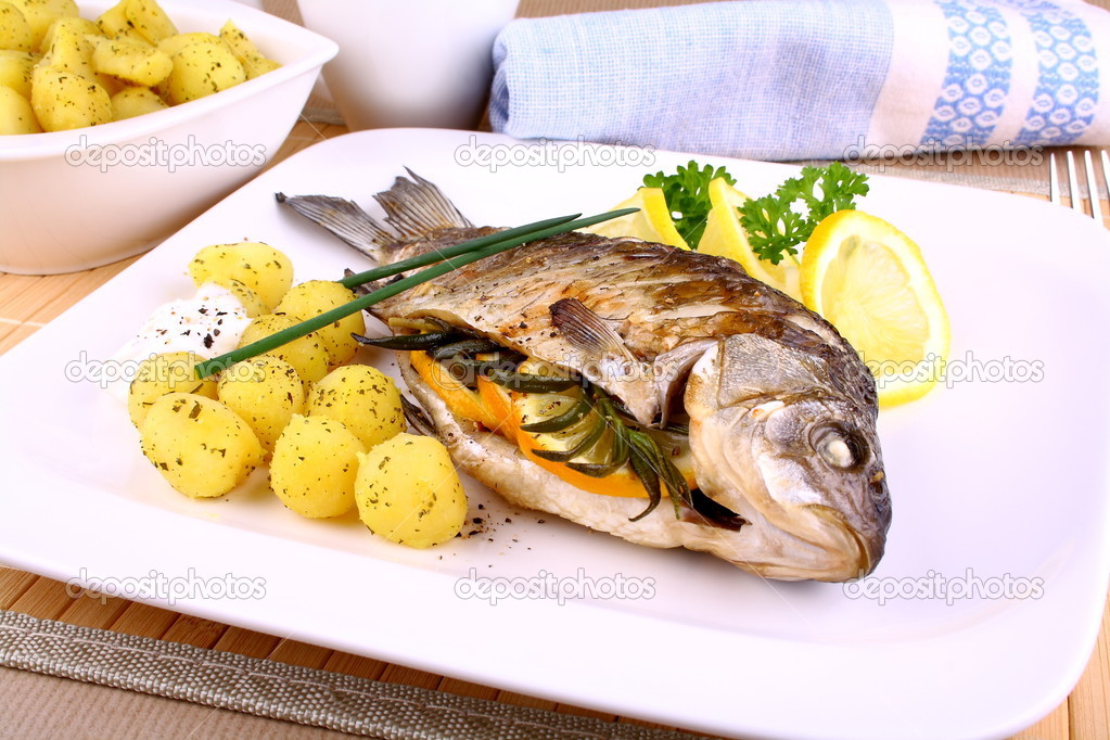 Whole grilled fish served with potatoes and lemon
