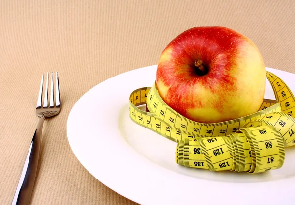 Tape measure and red apple on white plate with fork — Stock Photo, Image
