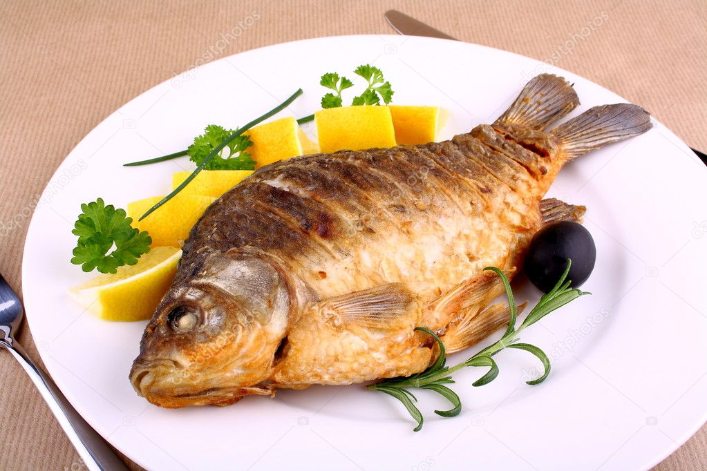 Fried carp on white plate with knife and fork