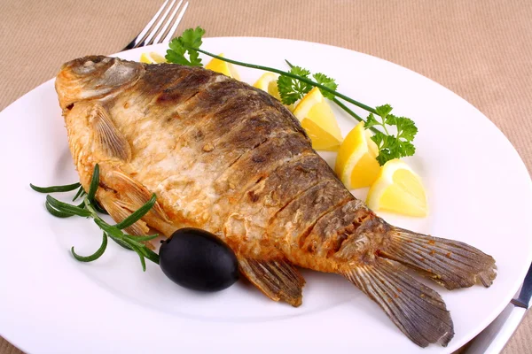 Fried fish on white plate with lemon, fork and knife — Stock Photo, Image