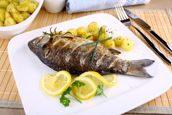 Grilled fish with potatoes, sauce, lemon and cutlery — Stock Photo, Image