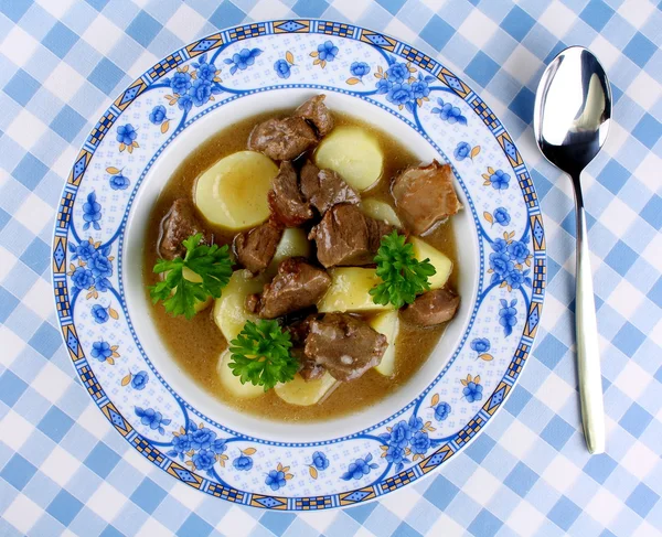 Gulaș sălbatic cu cartofi, sos și lingură pe placă albastră — Fotografie, imagine de stoc