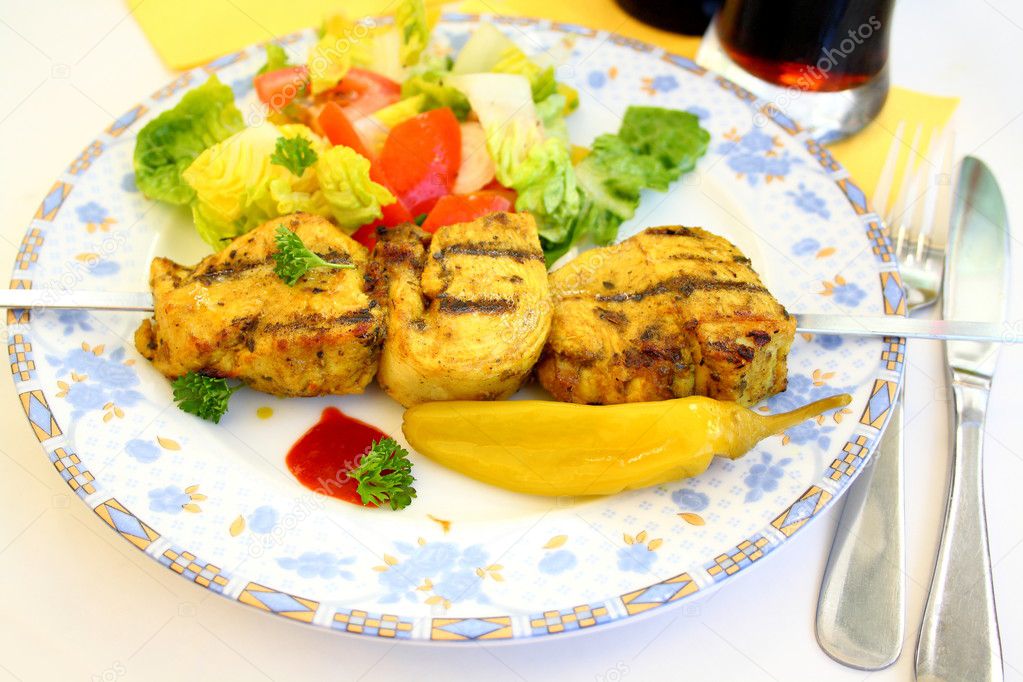 Grilled chicken fillet on metal skewer with salad, soft focus