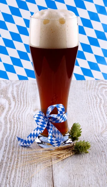 Dark wheat beer in glass with blue ribbon on white wood background