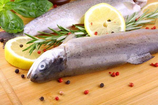 Due trote arcobaleno fresche, spezie e limone su tavola di bambù — Foto Stock