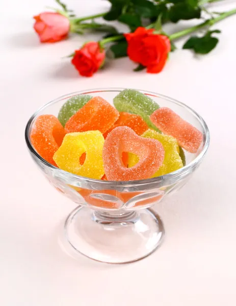 Colored candies with red hearts in glass bowl and roses — Stock Photo, Image