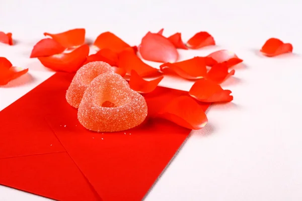 Two hearts from sugar candies on red envelope and petals — Stock Photo, Image