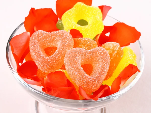 Colored candies with two red hearts in glass bowl and rose petals — Stock Photo, Image