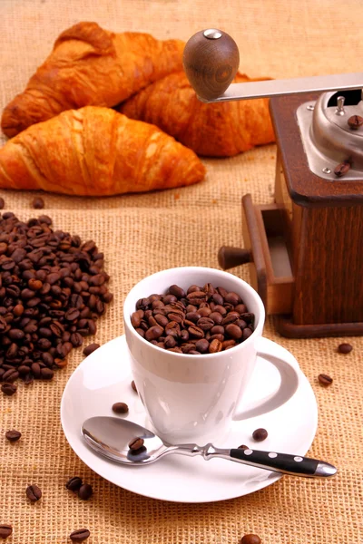 Grão de café em copo branco e croissant — Fotografia de Stock